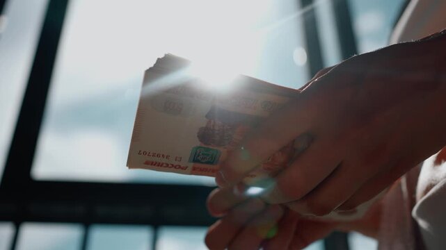 Close up of female hands counting a large stack of russian ruble currency against a bright window, symbolizing wealth, income, and successful financial transactions