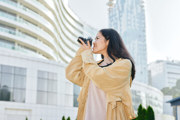 Fototapeta premium Woman with camera captures urban cityscape, fashion outerwear outdoors in a modern skyline setting, candid street photography focus and skyline backdrop for travel lifestyle and daily moments