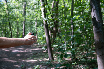 Hiker holding a canister of pepper spray while walking down a dirt trail in a sunny green forest. © olga