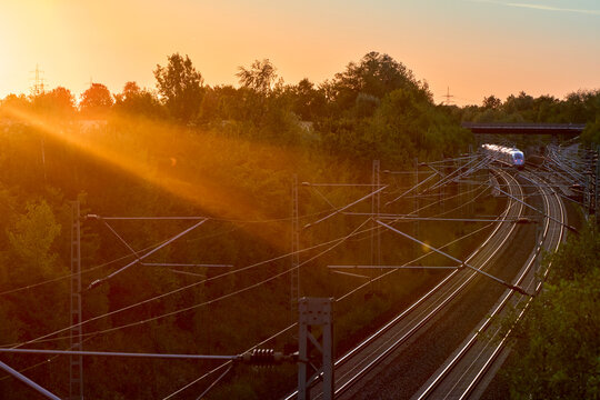 Intercity train traveling through a scenic railway corridor at sunset, surrounded by trees and overhead power lines. Stuttgart to Mannheim, Baden-W&uuml;rttemberg, Germany