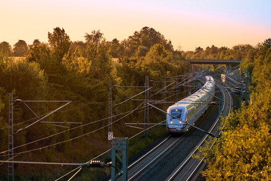 Intercity train traveling through a scenic railway corridor at sunset, surrounded by trees and overhead power lines. Stuttgart to Mannheim, Baden-W&uuml;rttemberg, Germany