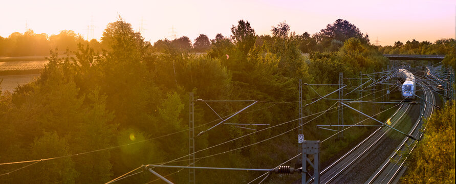 Intercity train traveling through a scenic railway corridor at sunset, surrounded by trees and overhead power lines. Stuttgart to Mannheim, Baden-W&uuml;rttemberg, Germany