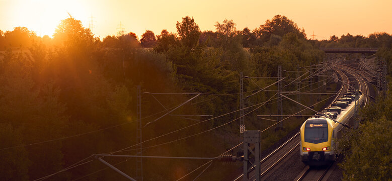 Intercity train traveling through a scenic railway corridor at sunset, surrounded by trees and overhead power lines. Stuttgart to Mannheim, Baden-W&uuml;rttemberg, Germany