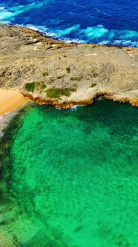 Rocky coastline of Mar Chiquita beach, Manati, Puerto Rico. Aerial drone perspective of limestone formations, turquoise water, and sandy shore under bright sunlight. Vertical video.