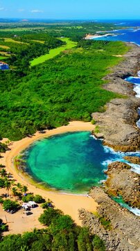 Aerial view of Mar Chiquita beach Puerto Rico. Elevated perspective of tropical vegetation, golden sand cove, and rocky cliffs bordering the Atlantic Ocean. Vertical video.