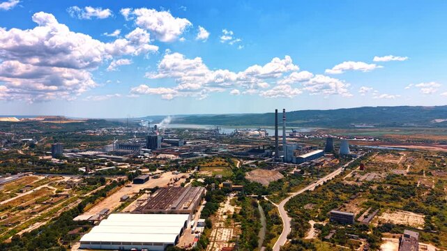 Industry view near river and mountains. Aerial view of an industrial area by a river surrounded by green hills under a blue sky with some clouds.