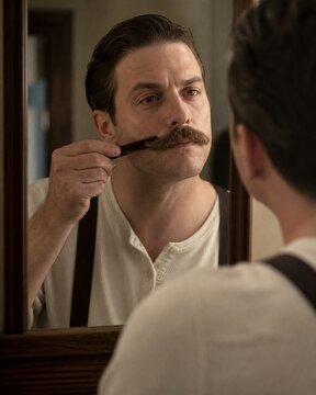 Man combing and styling his mustache while looking in a mirror