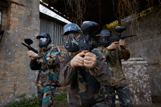Armed group of several soldiers practice with paintball weapons on training field, taking positions