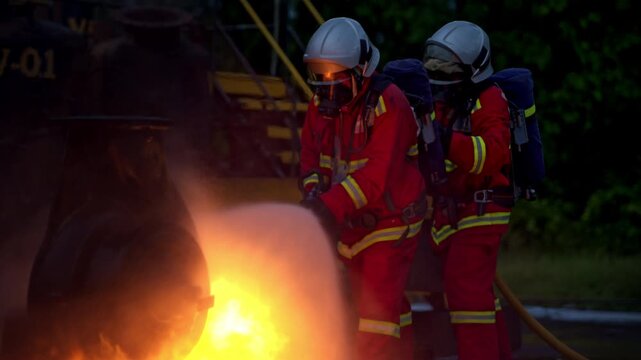 Firefighters use a water hose to suppress an industrial fire during emergency response training in a wet outdoor facility
