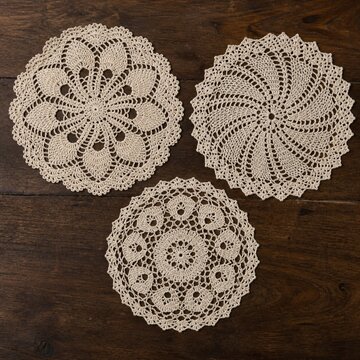 Three cream-colored crocheted doilies on dark wood background