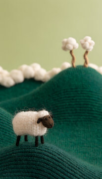 Miniature Knitted Wool Sheep Standing On Rolling Green Knit Fabric Hills With Cotton Puff Tree Clouds In Background Showing Handmade Felt Craft Landscape Cute Whimsical Textile Art Concept