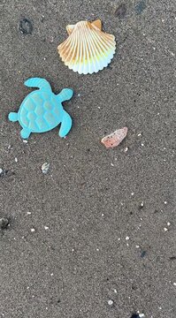 Top view of decorative sea turtle and seashell figures on wet beach sand, as sea wave foam washes in from the side leaving ample copy space for advertising.