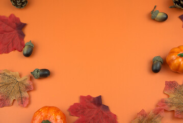 Autumn leaves, small pumpkins, and acorns framing an orange background, creating a festive fall and halloween design © Chloe
