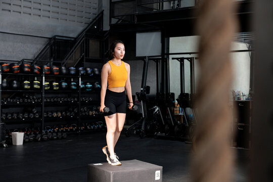 Woman steps onto plyometric box with dumbbells in a gym.