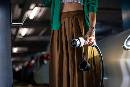 Hand holds electric car charging plug at a station.