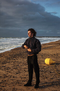 Young Man Stands on Beach With Waves and Drifting Buoy