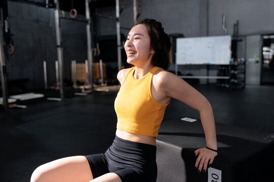 Laughing woman resting on plyometric box in gym