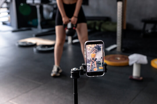 Woman filming kettlebell workout at gym with mobile phone on tripod