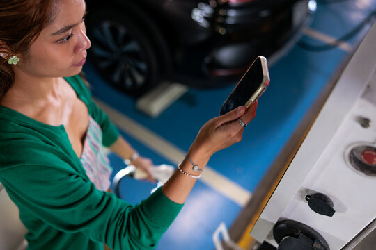 Woman uses mobile phone while charging electric vehicle.