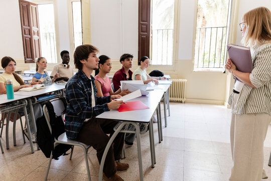 Diverse students attentively listening female teacher in classroom