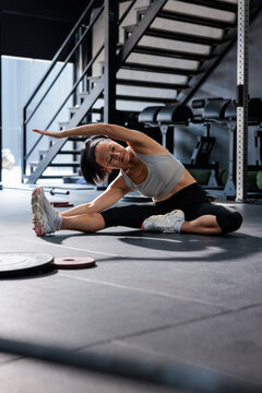 Woman performing seated side stretch in gym near stairs
