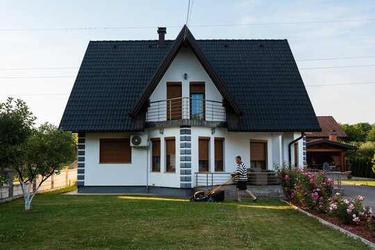Man mowing front lawn outside detached family home at golden hour