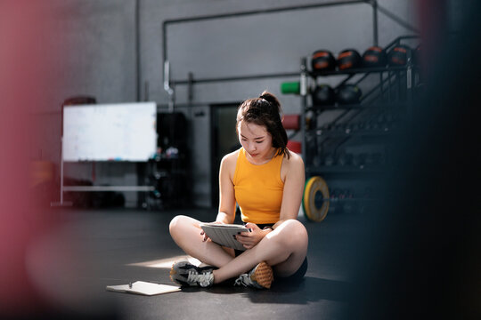 Woman with tablet sits cross-legged in gym.