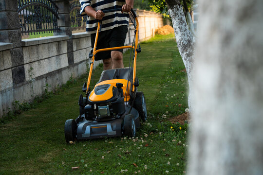 Close up of homeowner mowing narrow strip of backyard lawn