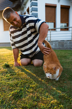 Man spending time with a ginger cat on a grassy lawn