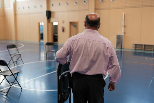 Man carrying folding chair preparing gymnasium for event