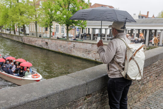 Man Tourist Under Umbrella Watching Canal Boat Tour in Bruges Belgium