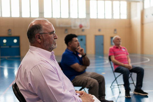 Men sitting in gymnasium listening to a presentation