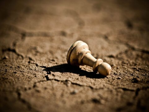 Fallen White Chess Pawn on Cracked Dry Ground Symbolizing Defeat or Despair