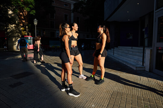 Three women exercise together on city street in evening light