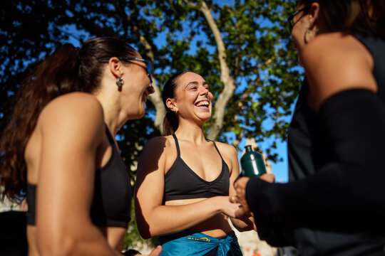 Friends laugh together during a sunny outdoor workout session