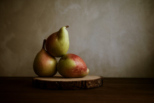 Three Pears Arranged on a Wooden Slice in Soft Light