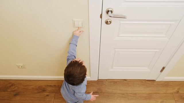 Child reaching to turn on electric light switch on wall. Little boy tapping power button at home. Indoor activities for toddler, safety and exploration in early childhood development.