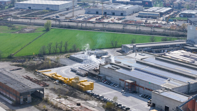 Pontenure, Italy - 30 March 2026: Aerial view of the YTONG Xella Italia factory with industrial buildings, rooftop solar panels, yellow material storage, and smoking vents.
