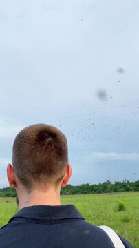 Midge hatching season. The insects fly through the air near a man's head, swarming against the backdrop of an overcast sky. Midges in spring, time-lapse footage