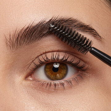 Extreme macro close up of woman eye with spoolie brush shaping perfect eyebrow