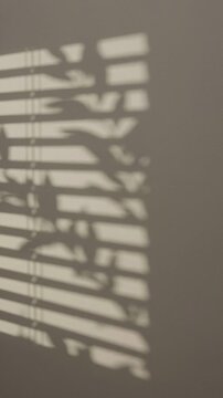 Abstract shadow of window blinds cast on a neutral beige wall background.