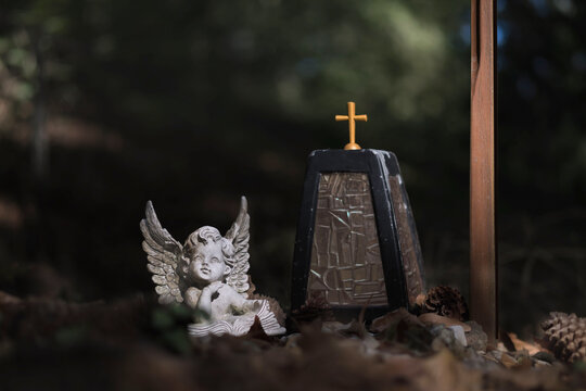 Kleine Engelsfigur mit Lampe und Kreuz als Helfer bei der Trauer am Grab auf dem Friedhof im Schatten