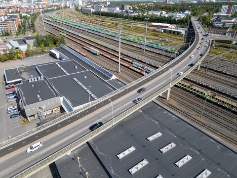 Oulu, Finland - 05 August 2026: Aerial view of a modern road bridge crossing over extensive railway tracks and freight trains in an industrial urban area.