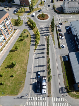 Oulu, Finland - 05 August 2026: Aerial view of a roundabout and road infrastructure in Oulu, featuring green spaces, parked cars, and long shadows cast by trees along the street.