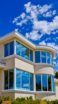 A modern curved building with large windows reflecting a blue sky and clouds