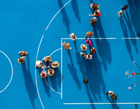 Belgrade, Serbia - 01 December 2025: Aerial view of children gathering and playing during a school recess on a blue outdoor basketball court.