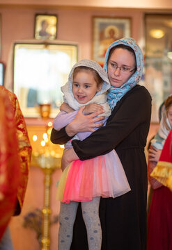 Mother brings her daughter to Communion in church, girl smiles happily.