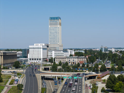 Krakow, Poland - 04 August 2026: Aerial view of the Unity Tower rising above the urban landscape with busy roads, traffic, and green trees under a clear blue sky.