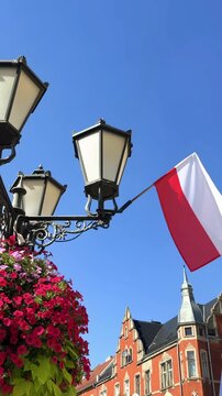 Decorative street lamp with colorful flower planters and Polish national flag on a city street, urban decoration and patriotic symbol in Poland during summer