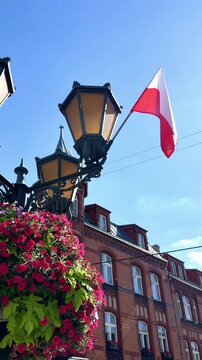Decorative street lamp with colorful flower planters and Polish national flag on a city street, urban decoration and patriotic symbol in Poland during summer